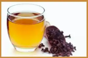 A glass of clove water on a wooden table, used as a natural morning detox drink.