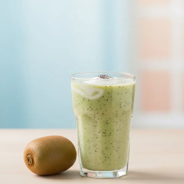 A professional health blog style photo of a fresh kiwi smoothie in a glass with a whole kiwi fruit on a soft pastel background, highlighting prenatal nutrition.
